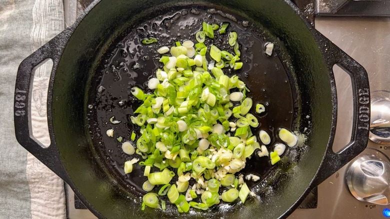 Minced garlic and sliced scallions in cast iron pan on stovetop