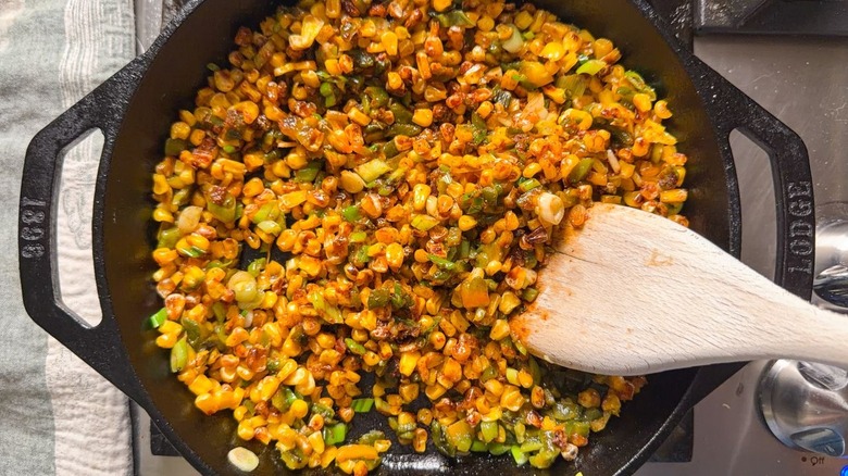 Roasted corn, poblano peppers, and scallions with seasonings in cast iron skillet on stovetop