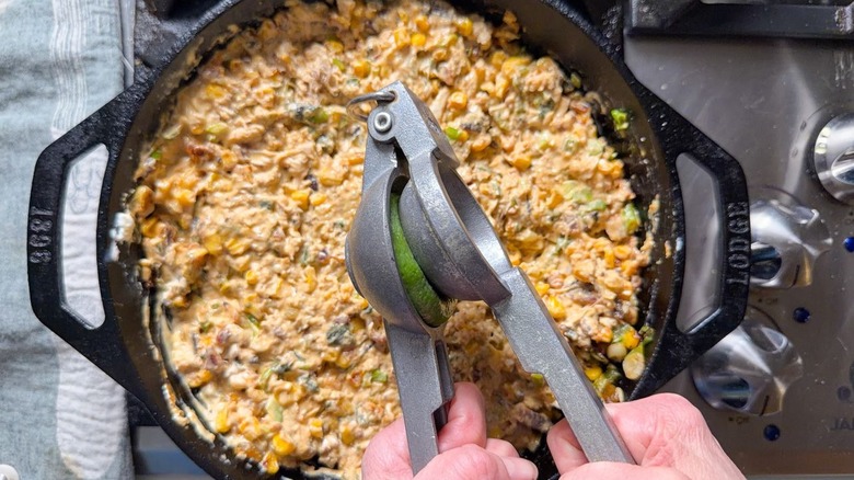 Squeezing fresh lime juice into cheesy crab dip in cast iron skillet on stovetop