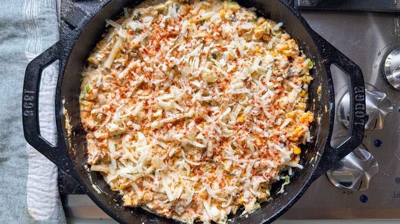 Unbaked cheesy crab dip with shredded cheese and smoked paprika in cast iron skillet on stovetop