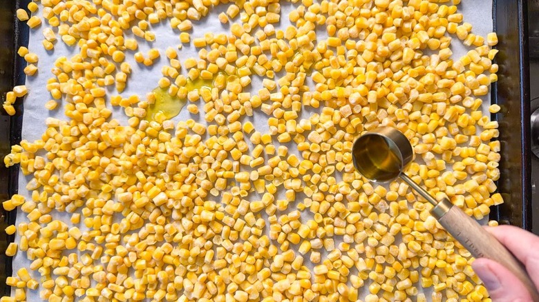 Drizzling olive oil on corn kernels on a parchment-lined baking sheet
