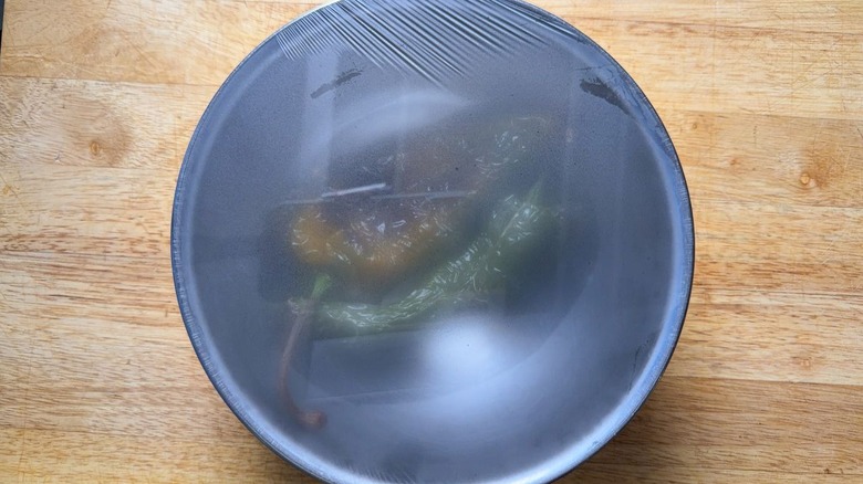 Poblano peppers steaming in plastic-covered stainless steel bowl