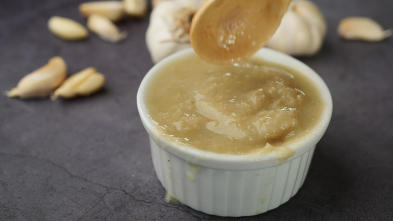 Small white bowl of garlic paste with wooden spoon being dipped in