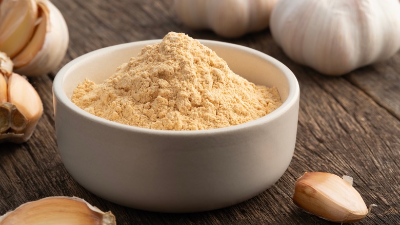 White bowl filled with garlic powder next to garlic cloves