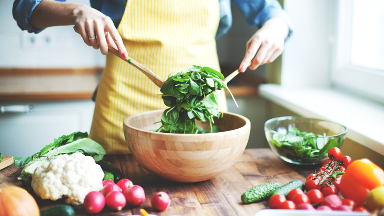 Hands toss a wooden bowl filled with spinach.