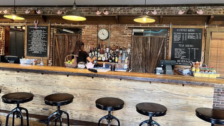 The wooden bar with bar stools, hanging lamps, and a red brick backsplash at Little Easy Cafe