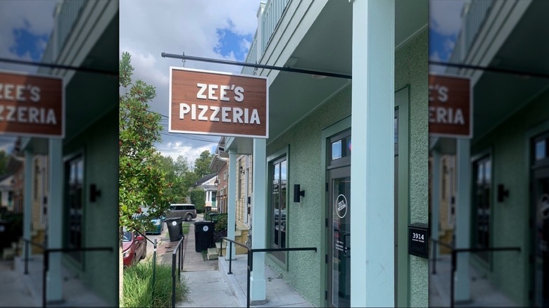 Exterior of Zee's Pizzeria with a sign hanging above the door