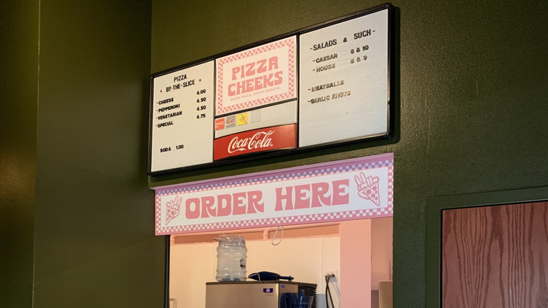 The main take-out counter at Pizza Cheeks with a pink and white sign