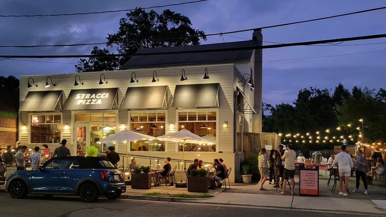 Exterior of Stracci Pizza, including patio, lit with fairy lights and bustling with people on a summer evening