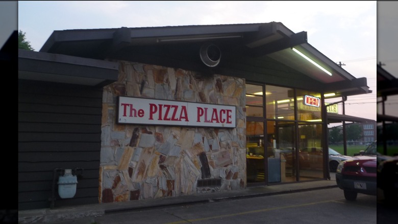 Exterior of The Pizza Place with a red and white sign on a stone wall