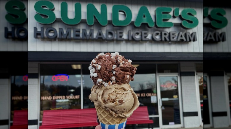 Cone of ice cream with two different flavor scoops in front of the storefront for Sundae's Homemade Ice Cream