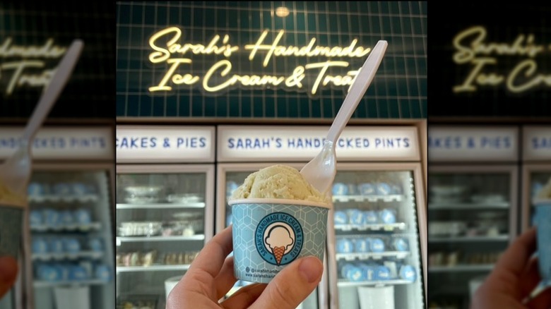 Hand holding a cup of white ice cream in front of the freezer at Sarah's Handmade Ice Cream