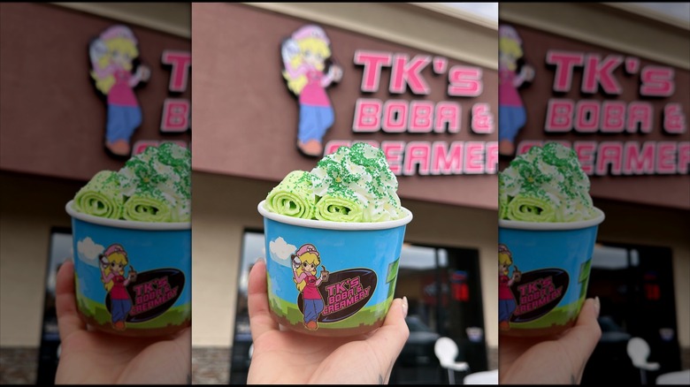 Hand holding cup of green rolled ice cream in front of TK's Boba & Creamery storefront
