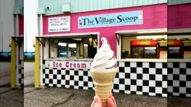 Hand holding a soft-serve ice cream cone in front of The Village Scoop