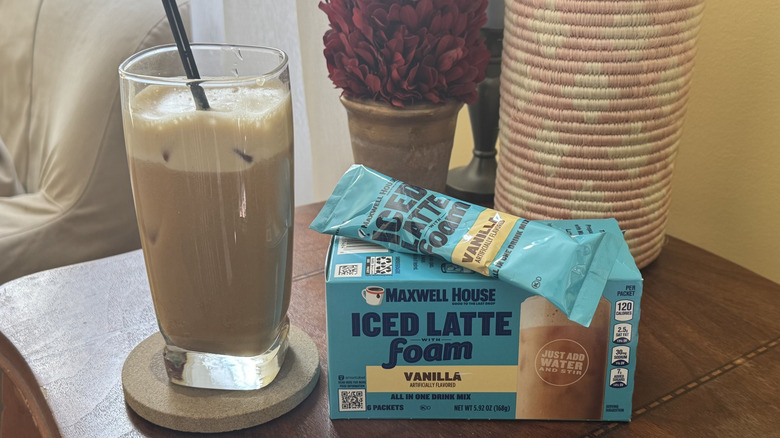 A cup of iced latte sitting next to a package of Maxwell House Iced Latte Foam packets