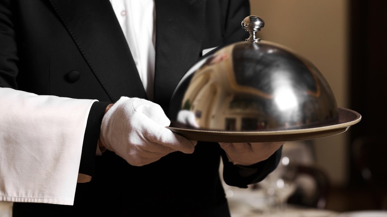 Fancy waiter carrying covered dish