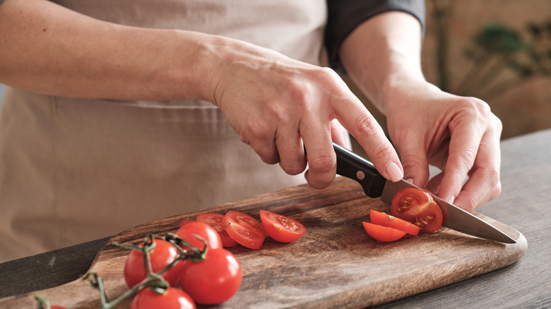 Hands use a paring knife to cut small tomatoes on the vine