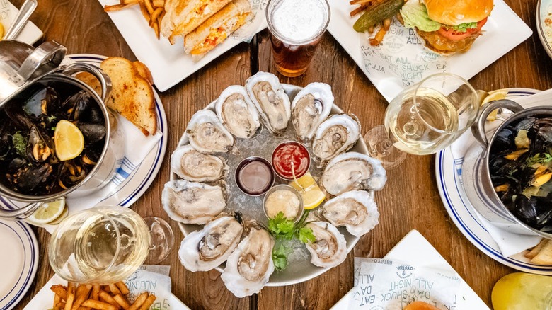 Overhead view of table with assortment of dishes including oysters and a burger with drinks