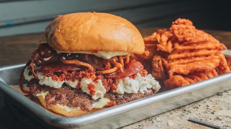 Smashburger with crumbly cheese and waffle fries on silver tray
