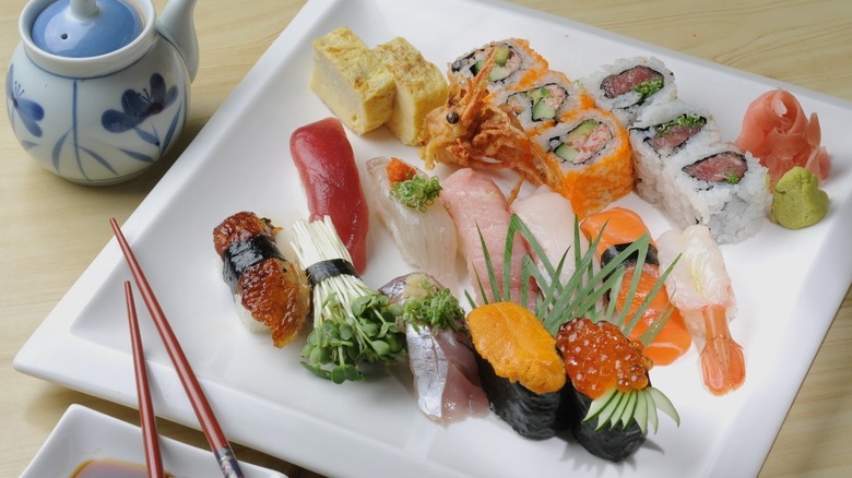 Square, white plate with assorted pieces of sushi and chopsticks