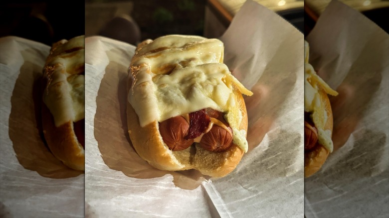 Double hot dog on bun with cheese, bacon, and sauces