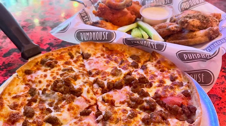 Pizza and basket of chicken wings with celery on red table