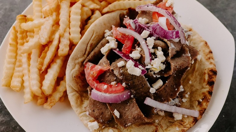 Gyro with feta, onions, tomatoes, and fries on plate