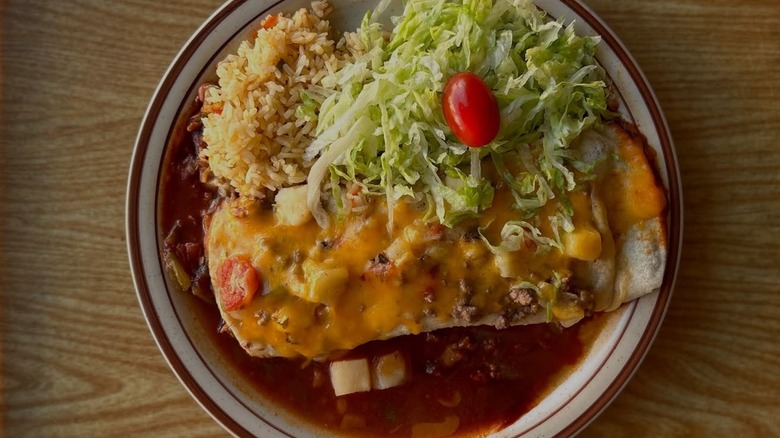 Wet burrito on plate with lettuce, cherry tomato, and rice