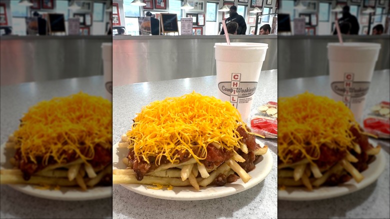 Plate of chili over fries with crackers and drink in background