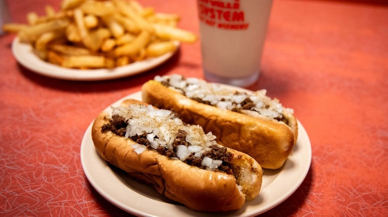 Two hot dogs on plate with fries and drink blurred in background