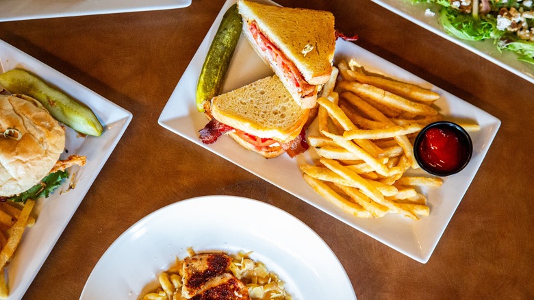 Assorted dishes on table with focus on BLT with fries, ketchup, and pickle