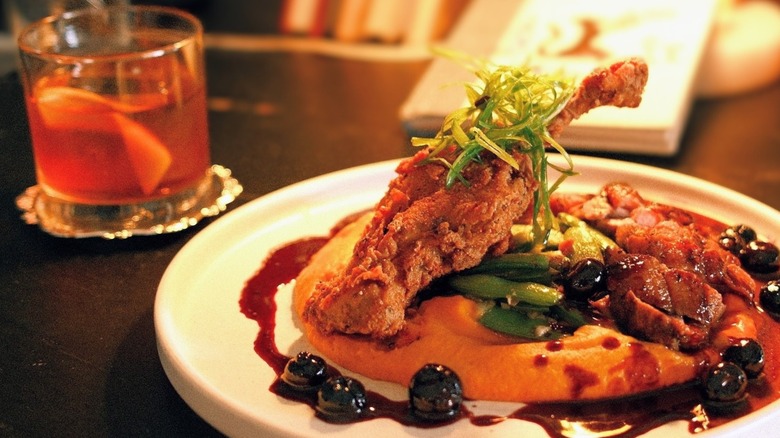 Duck on purée with Old Fashioned cocktail blurred in background