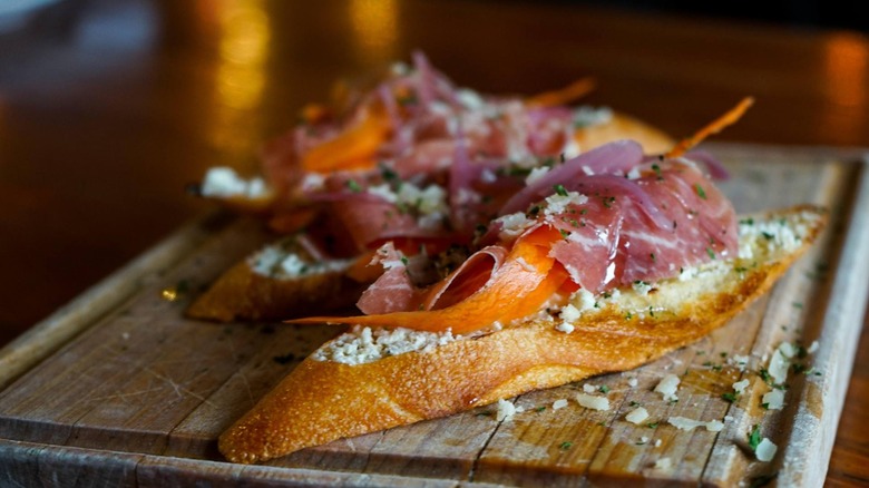 Slices of bread topped with thin-sliced meats and cheese on wooden board
