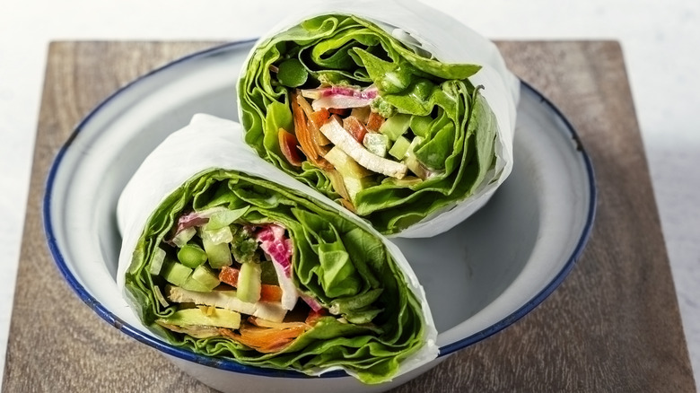 Two halves of a lettuce wrap sitting in a bowl on a wooden tabletop