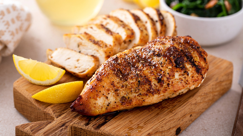 A whole seasoned and browned chicken breast beside a sliced version on a cutting board.