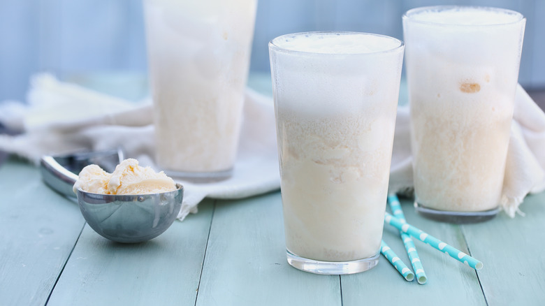 Three Boston Cooler ginger ale floats on a blue/green tabletop with an ice cream scooper full of vanilla ice cream in the foreground.