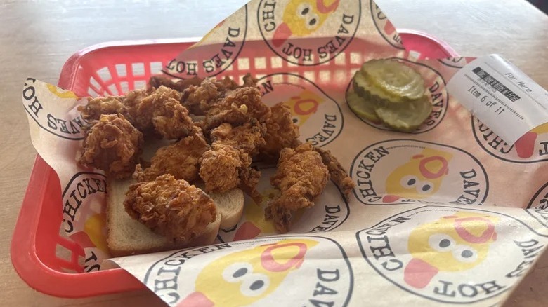 A basket of Dave's Hot Chicken bites with pickles and white bread.