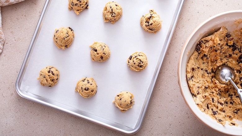 Raw chocolate chip cookie dough balls on a parchment lined baking sheet