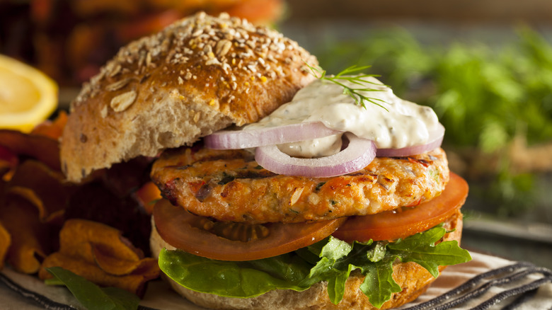 Salmon burger on a bun with sauce, lettuce, tomato, and onion.