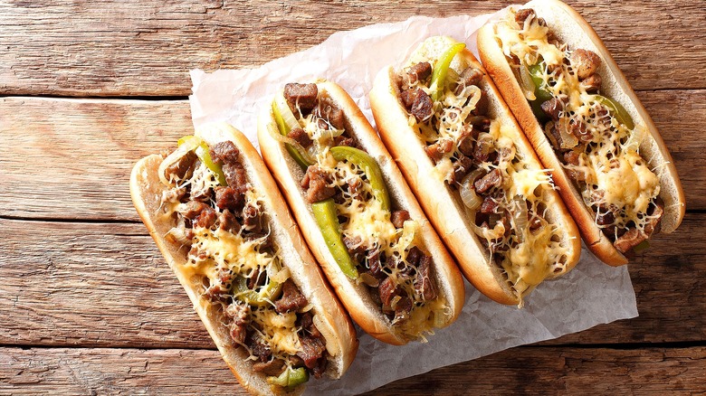 Four Philly cheesesteak sandwiches with steak, sliced onions, green peppers, and melted white cheese