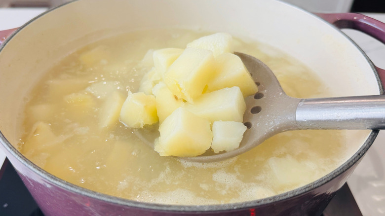 Slotted spoon holding chopped potatoes in over large pot