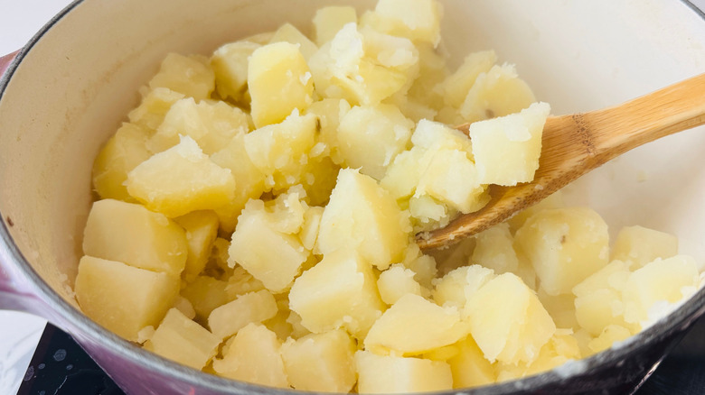 Chopped potatoes and wooden spoon in large pot