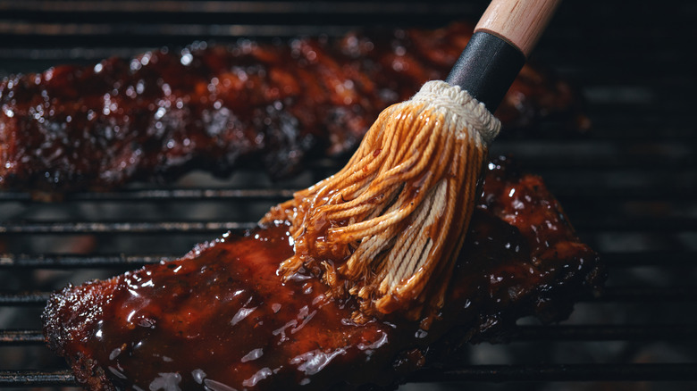 Barbecue sauce is brushed on ribs on a grill