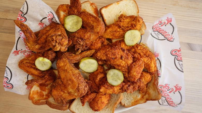 Pieces of hot fried chicken and pickles on white bread with branded paper.