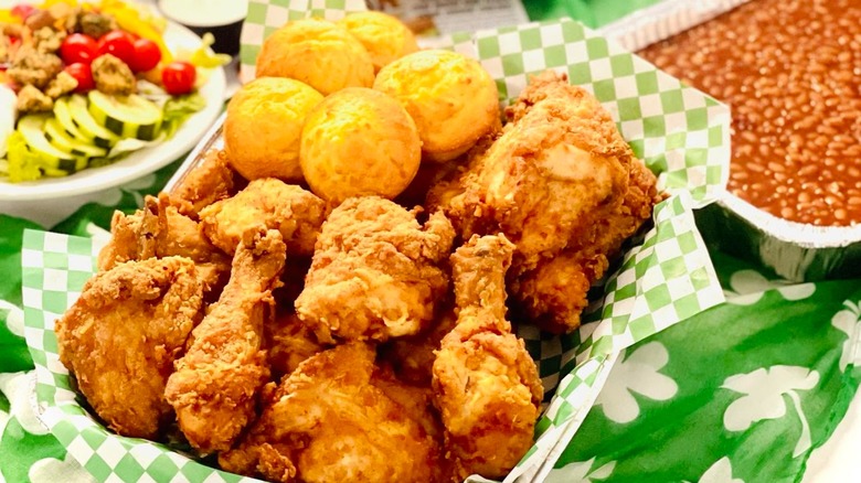 Tray of fried chicken and cornbread with sides of baked beans and salad.