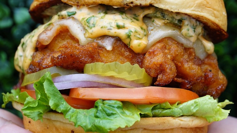 Fried chicken sandwich with sauces, onions, tomato, and lettuce.