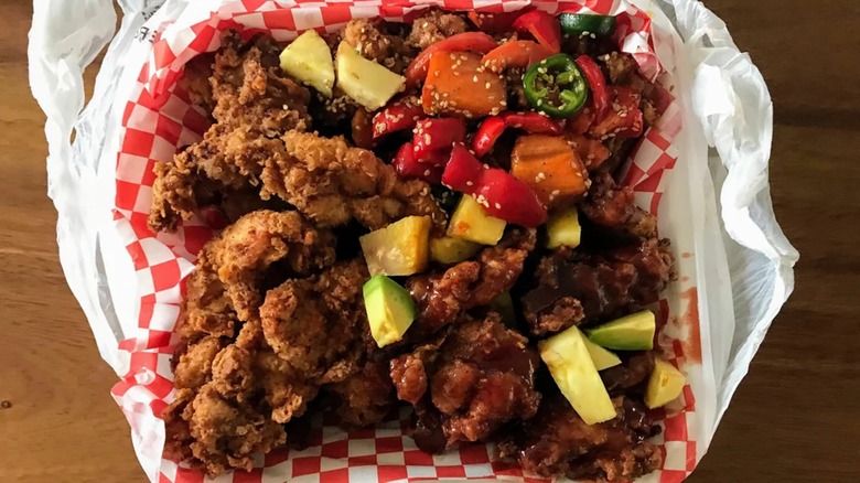 Crunchy fried chicken in takeout container with fresh fruit and veg.