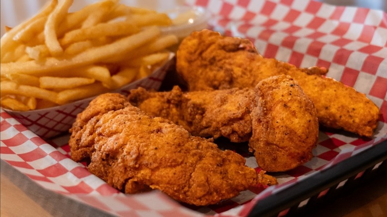 Chicken tenders on red and white checkered paper with french fries.
