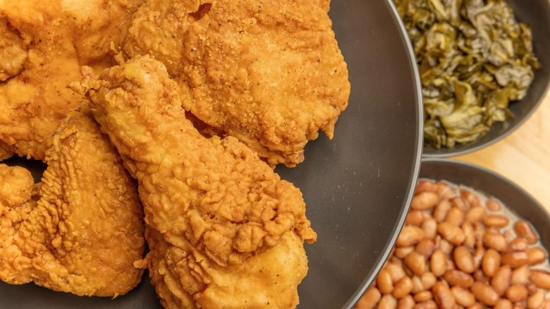 Plate of fried chicken with baked beans and collard greens blurred in background.