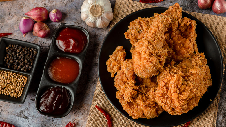 Plate of fried chicken with multiple sauces, seasonings, and garlic.